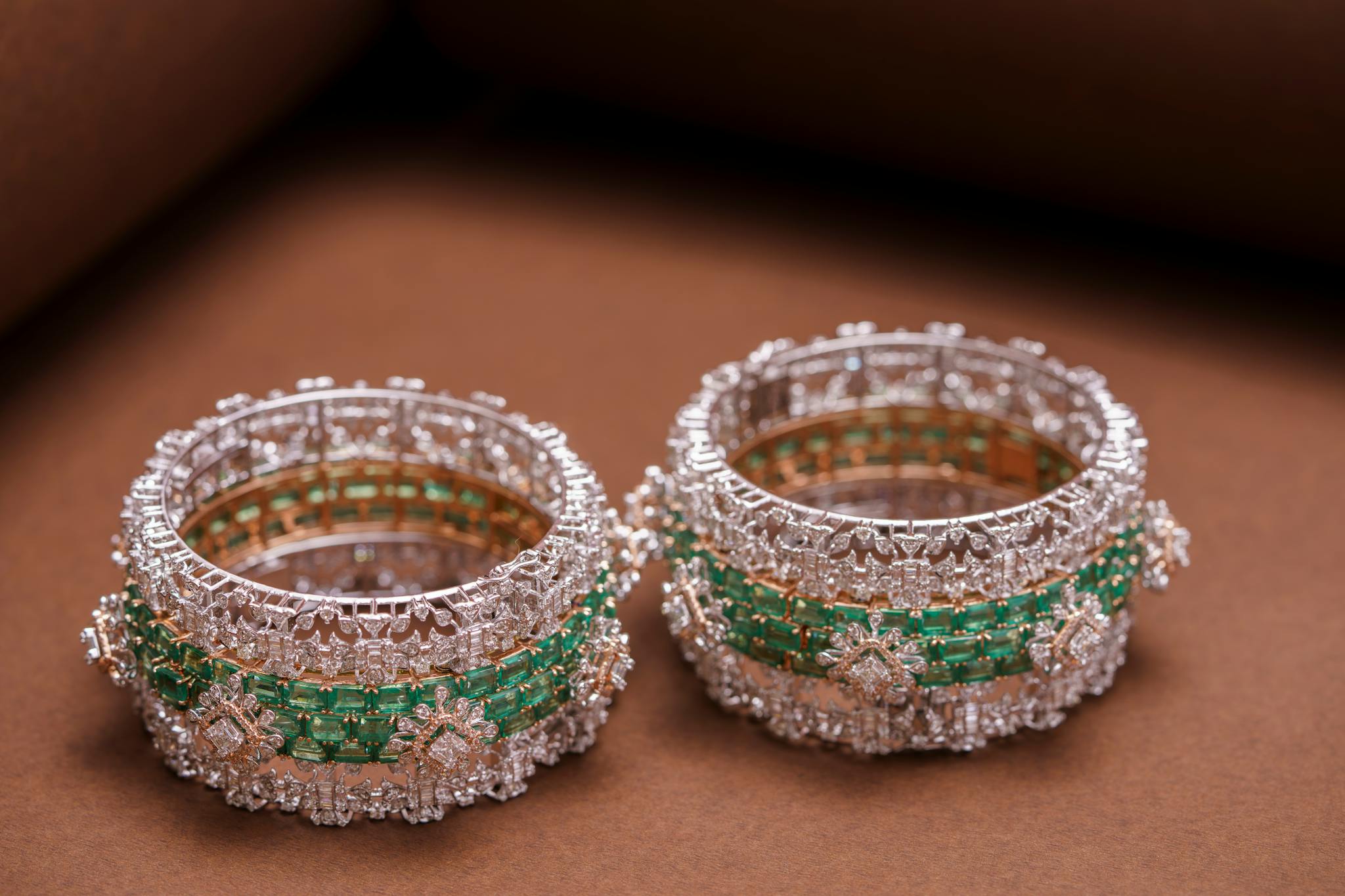 Two exquisite diamond and emerald bangles showcased with intricate detailing.